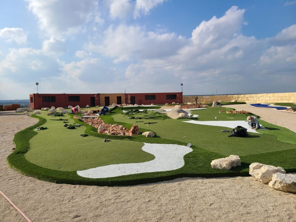 Crew installing synthetic turf greens beside the clubhouse buildings