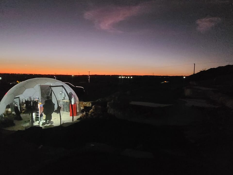 Geodesic dome clubhouse glowing at dusk against an orange Texas horizon