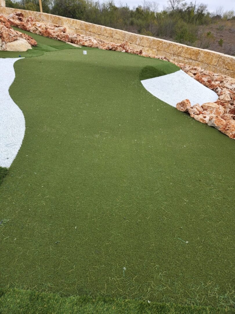 A contoured green with white sand pockets beside a limestone block wall.