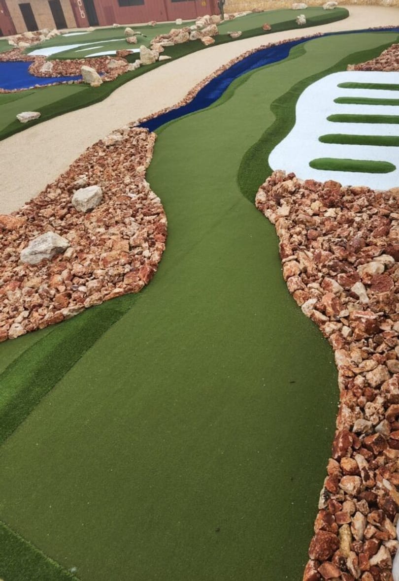 Blue water channel curving through hole six beside striped white sand