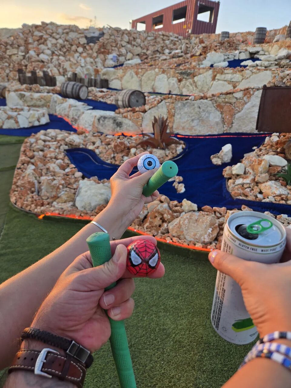 Two guests holding putters and a cold drink on the course at sunset