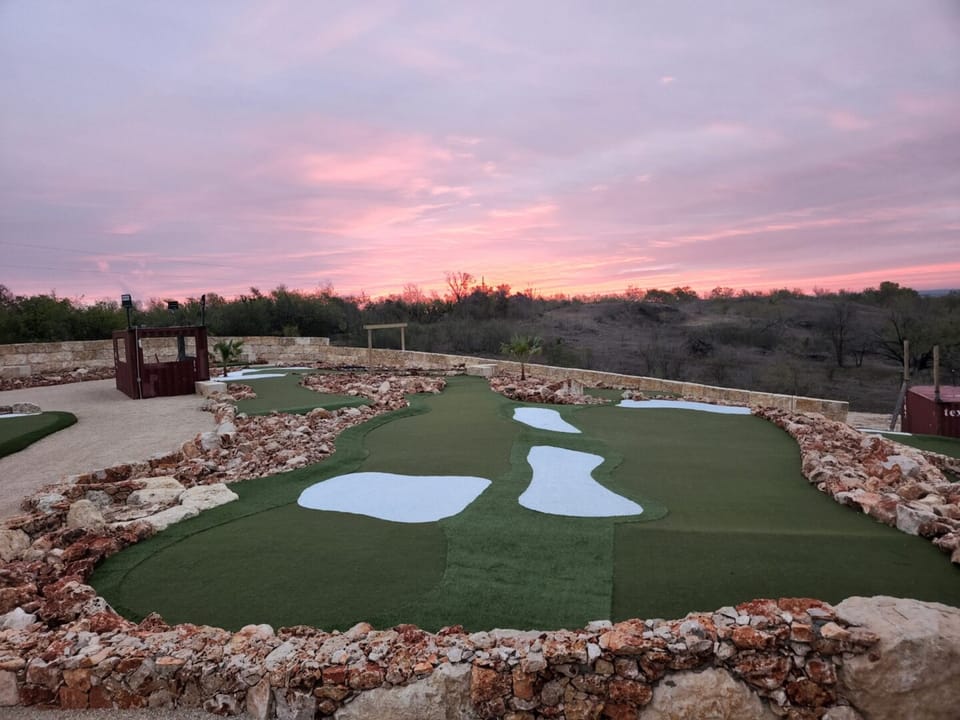 Putting green edged in rust rock under a pink Hill Country sunset